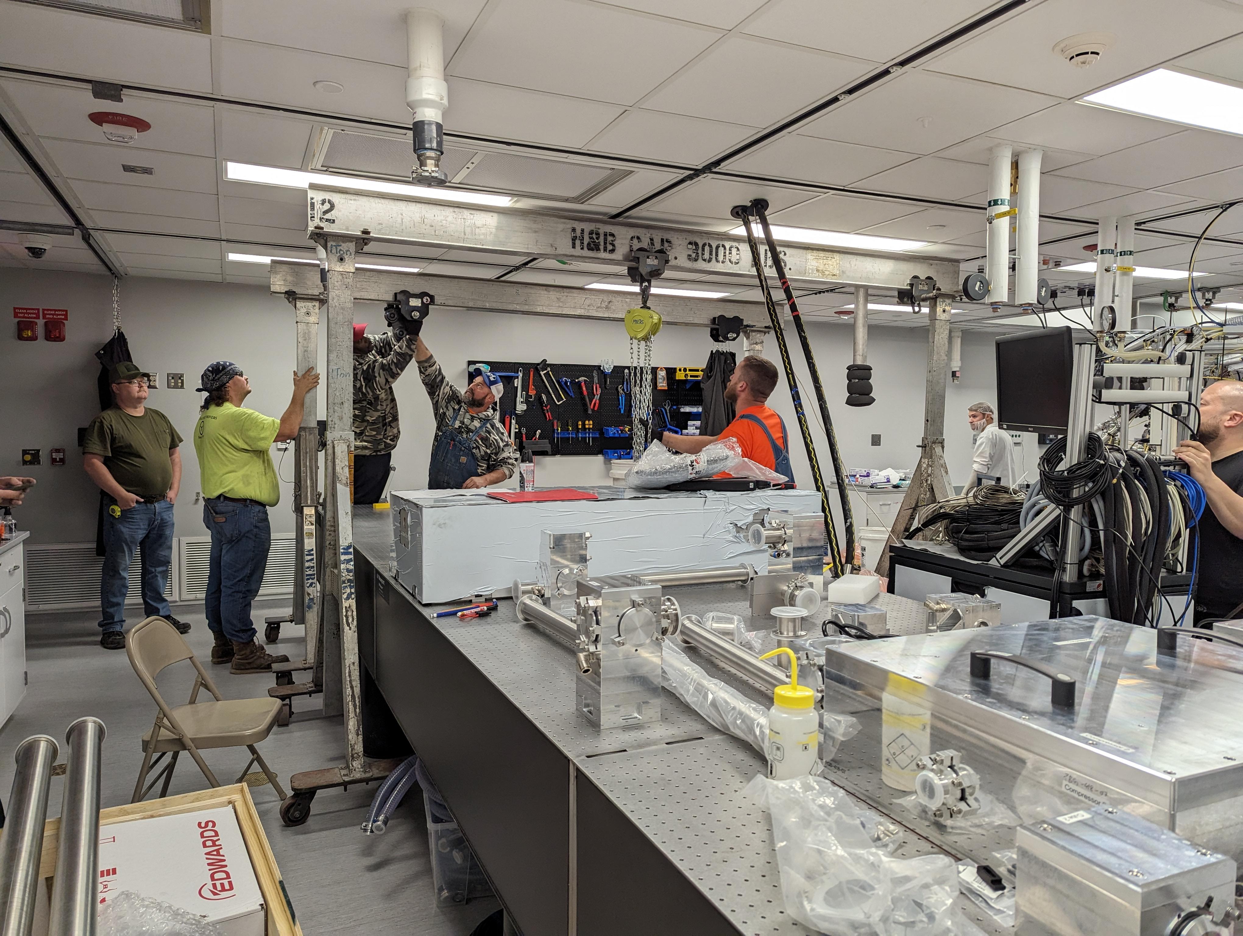 Workers using a hydraulic gantry to place laser components on a table in the NeXUS lab.