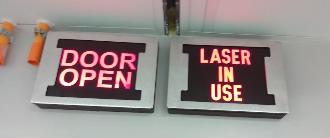 Two illuminated signs, one saying Door Open and one saying Laser In Use