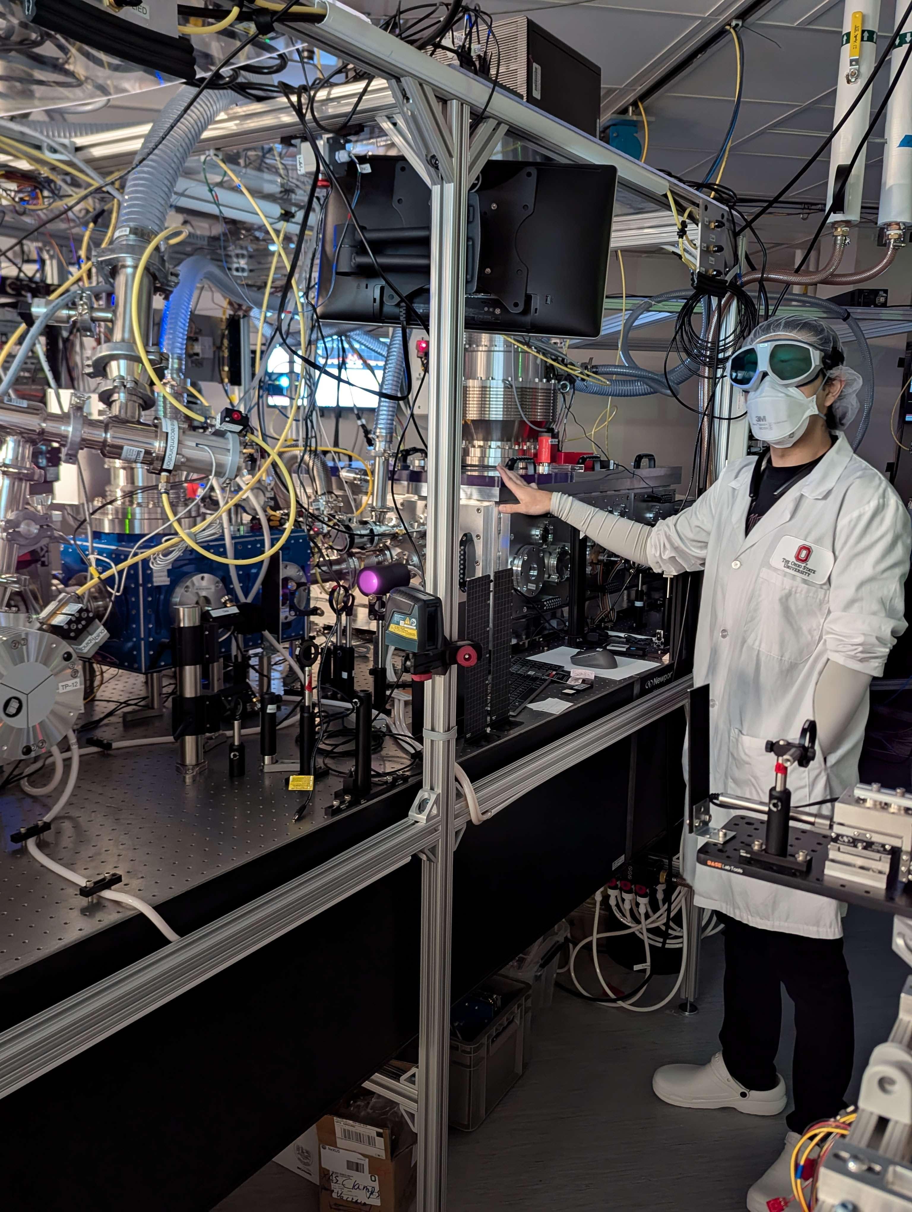 Scientist in a lab coat standing beside a laser table