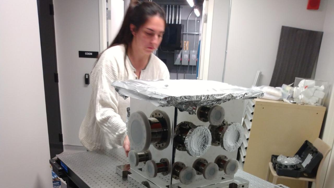 A graduate student rolls a piece of laboratory equipment on a cart.